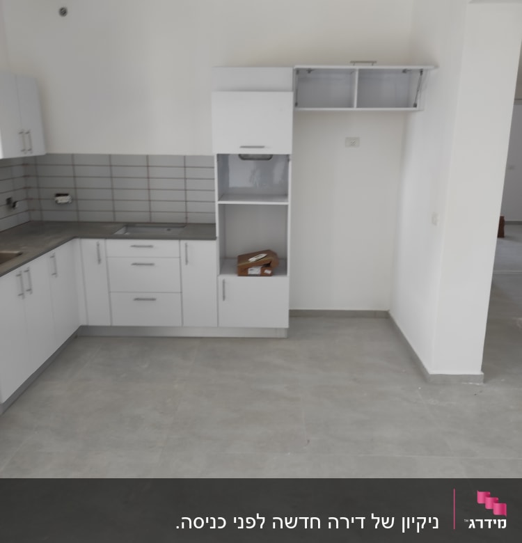 מטבח ריק עם ארונות לבנים ורצפה נקייה